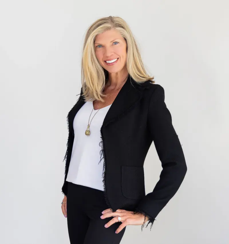 Amy Nakos smiling in a black blazer against a light studio background
