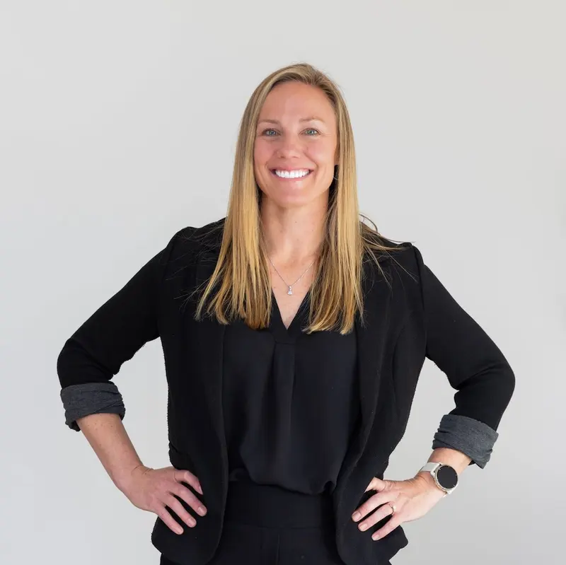 Candice De smiling in a black blazer against a light studio background